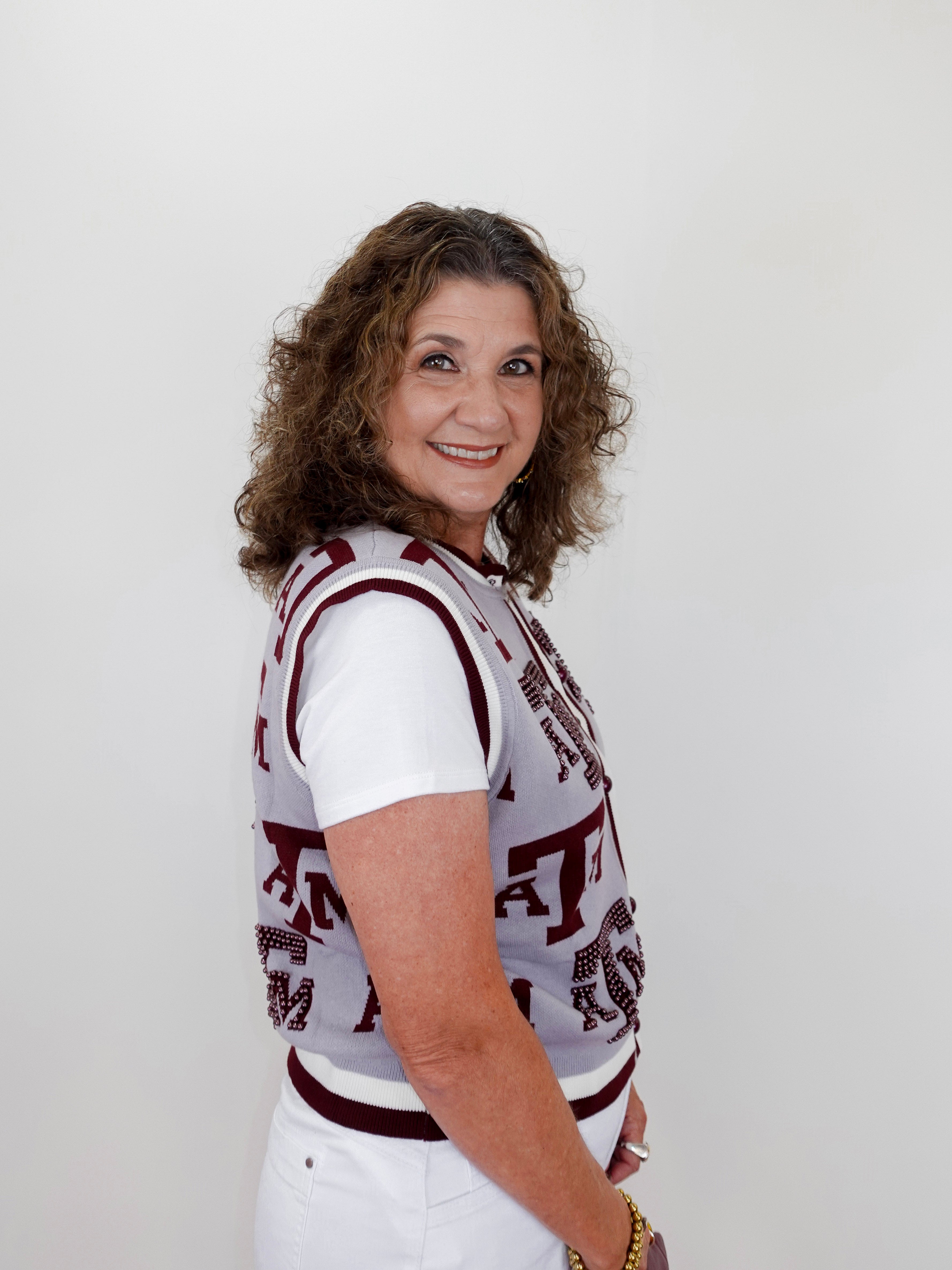 Woman wearing a patterned top and white pants against a plain background