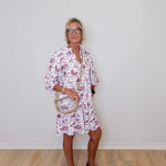 Woman wearing a white dress with red floral pattern against a plain white wall.
