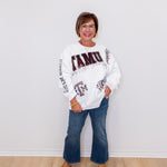 Woman wearing a white sweatshirt with text and graphics, standing against a white wall.