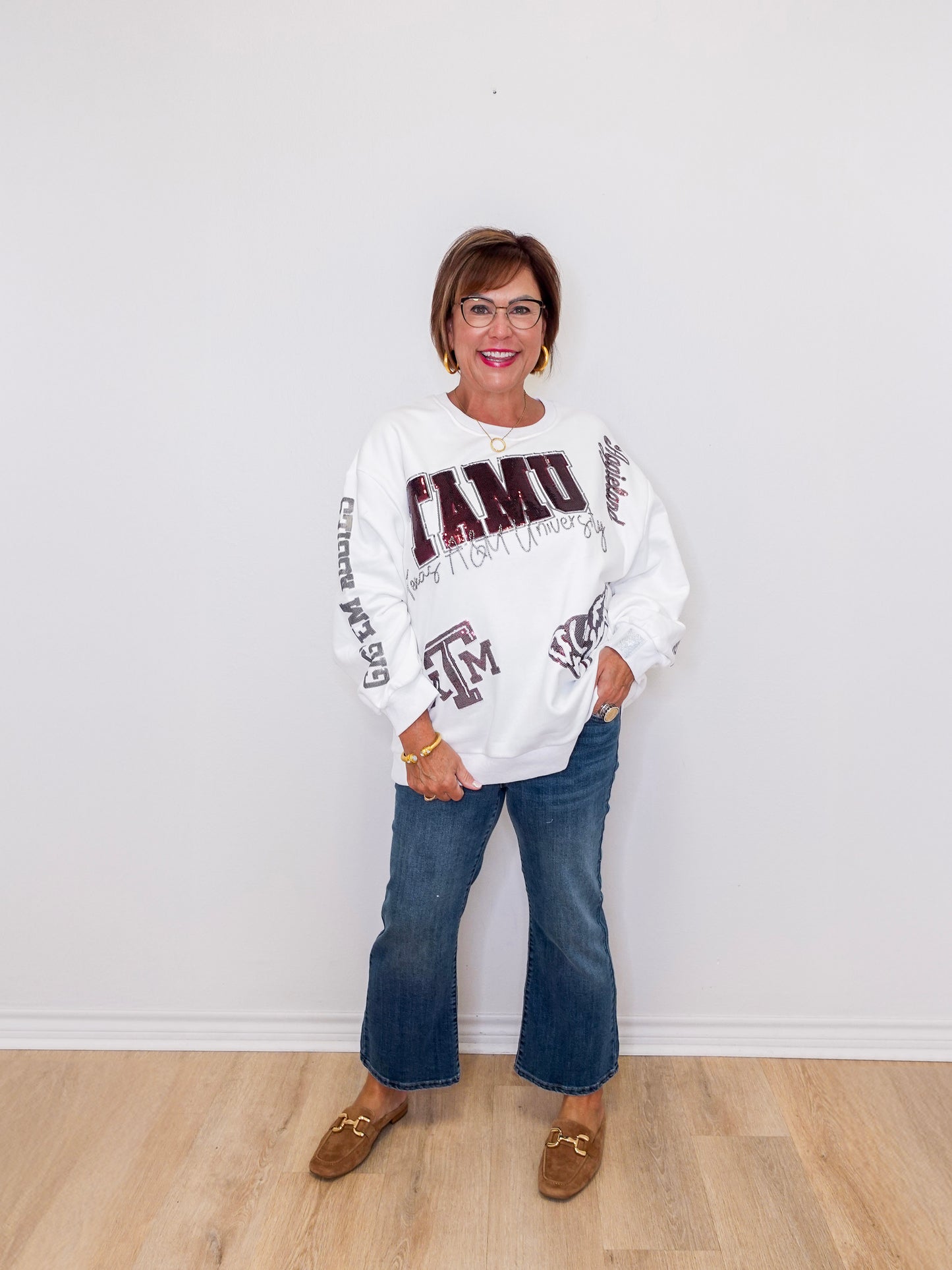 Woman wearing a white sweatshirt with text and graphics, standing against a white wall.
