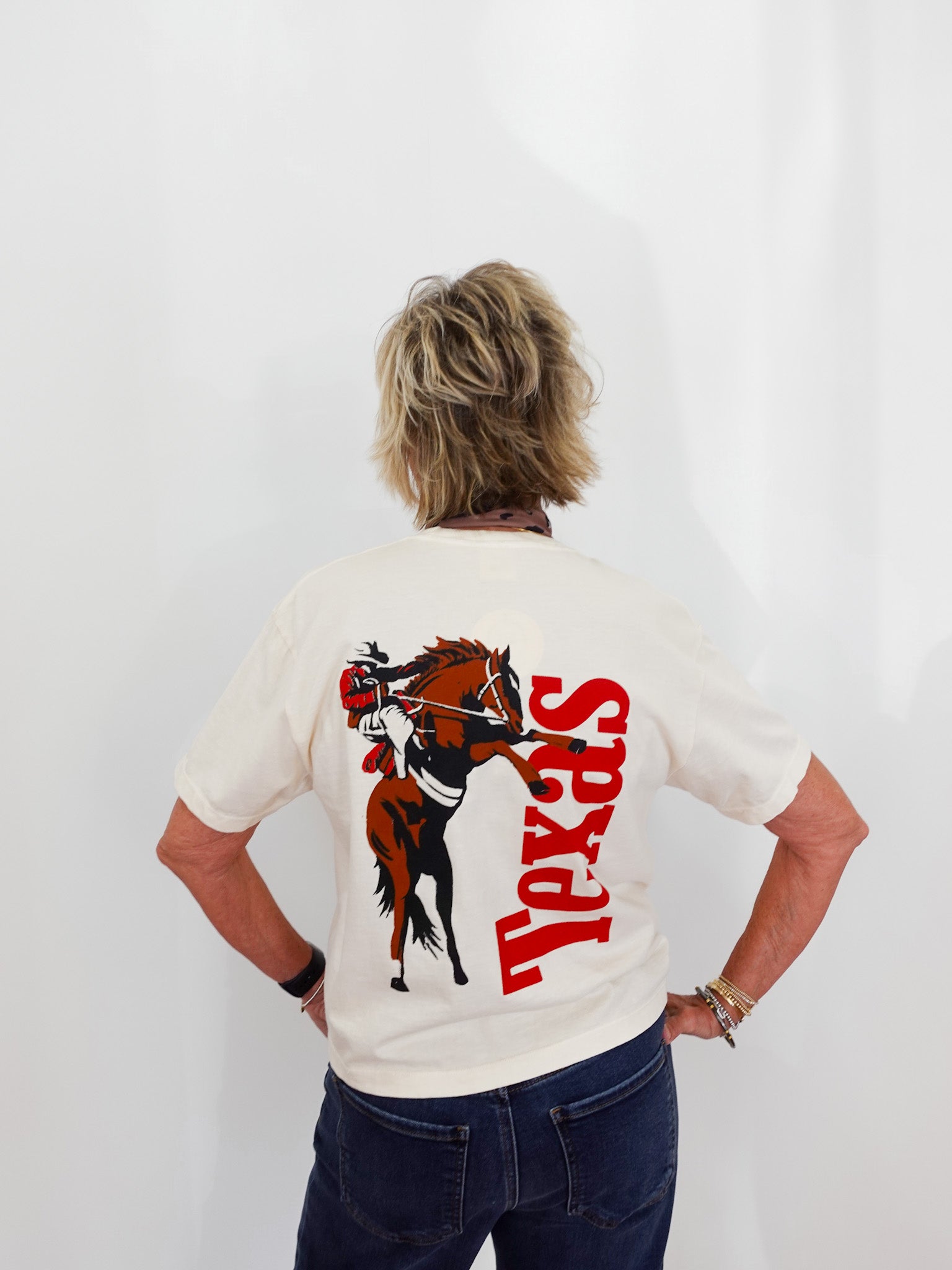 Person wearing a white t-shirt with a horse graphic and 'Texas' text on the back, standing against a plain background.