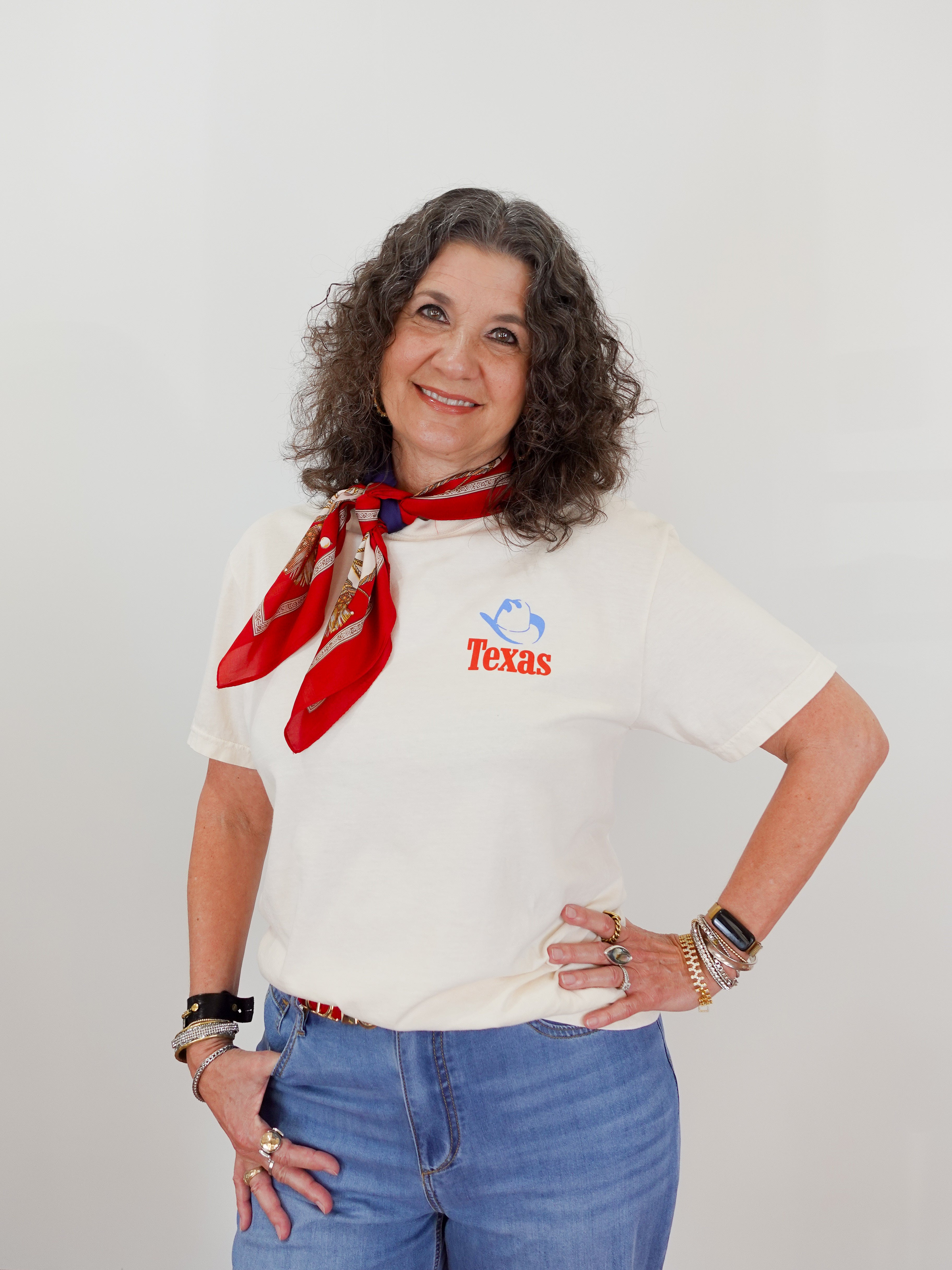 Woman wearing a white t-shirt with 'Texas' text, blue jeans, and a red scarf against a plain background