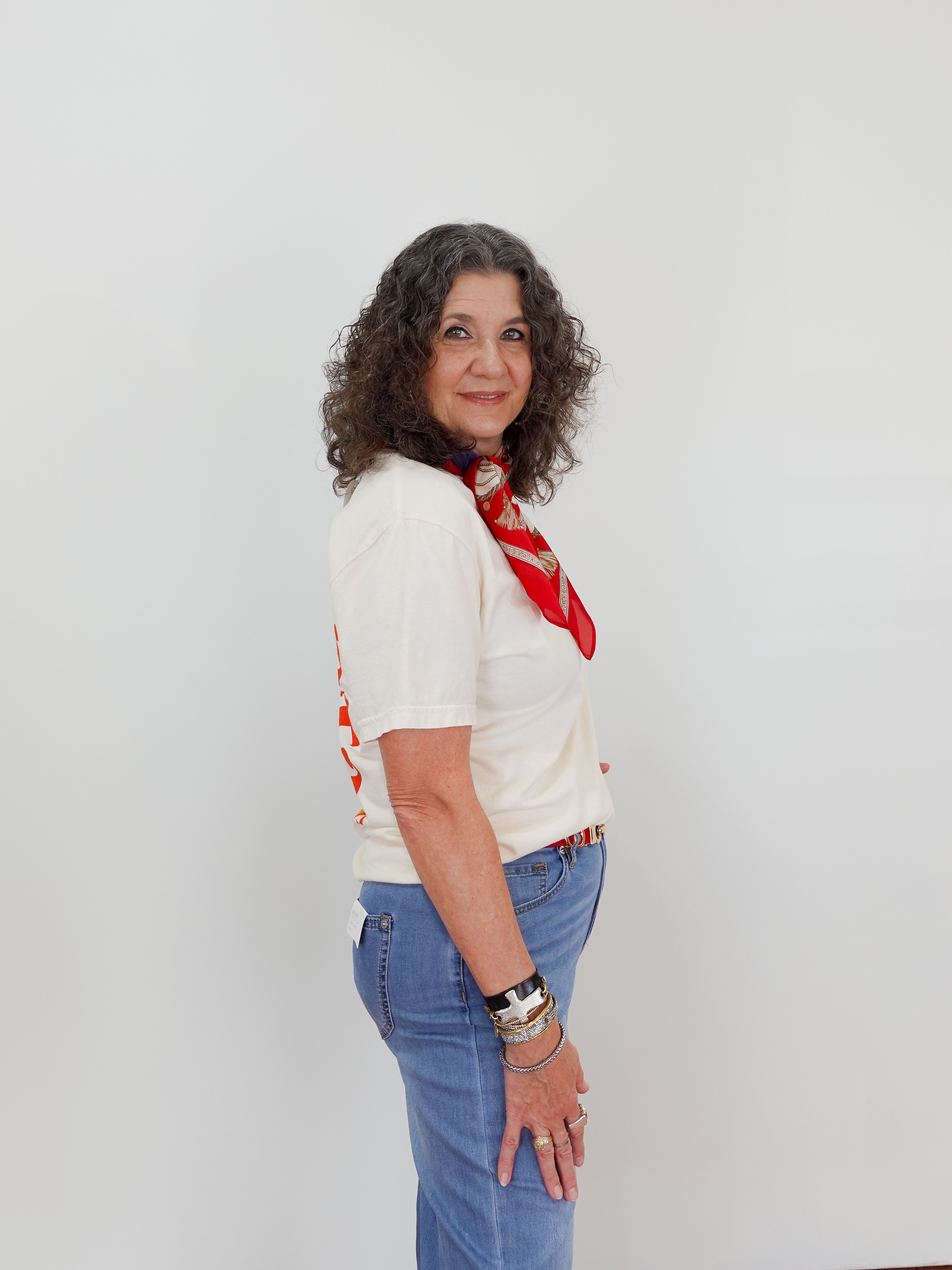 Woman wearing a white shirt, blue jeans, and a red scarf against a plain background