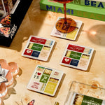 Matchbooks with various designs on a wooden surface with a glass of red wine.