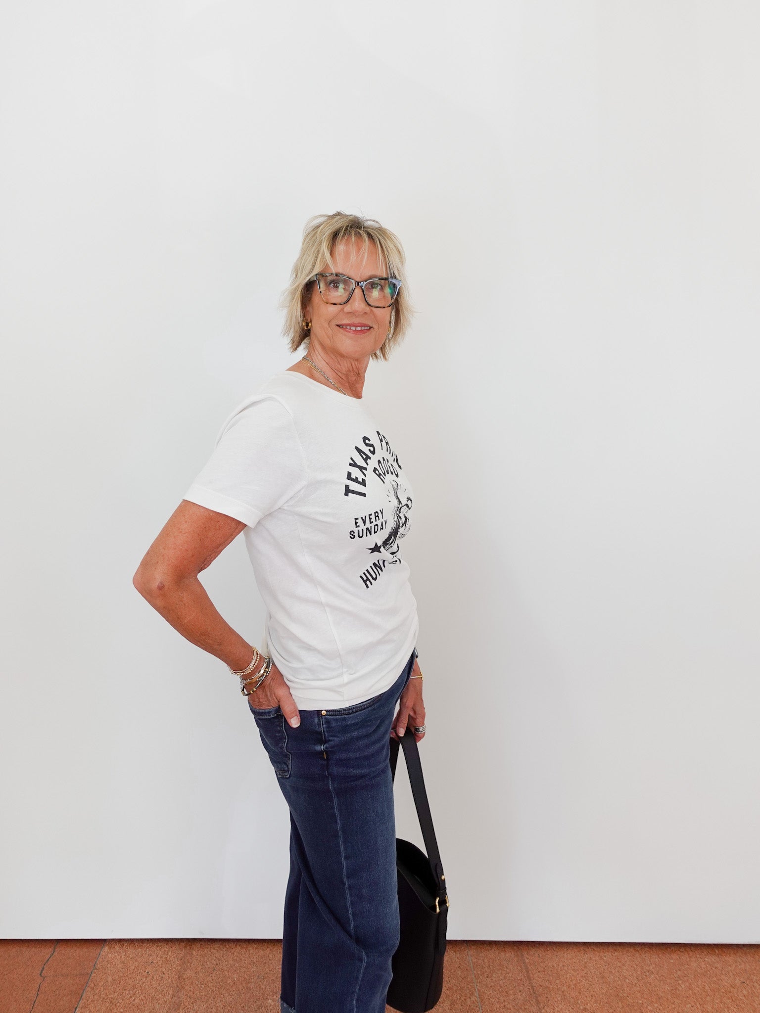 Woman wearing a white t-shirt with text and blue jeans against a white wall.