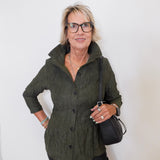 Woman wearing a green jacket and black pants against a white background