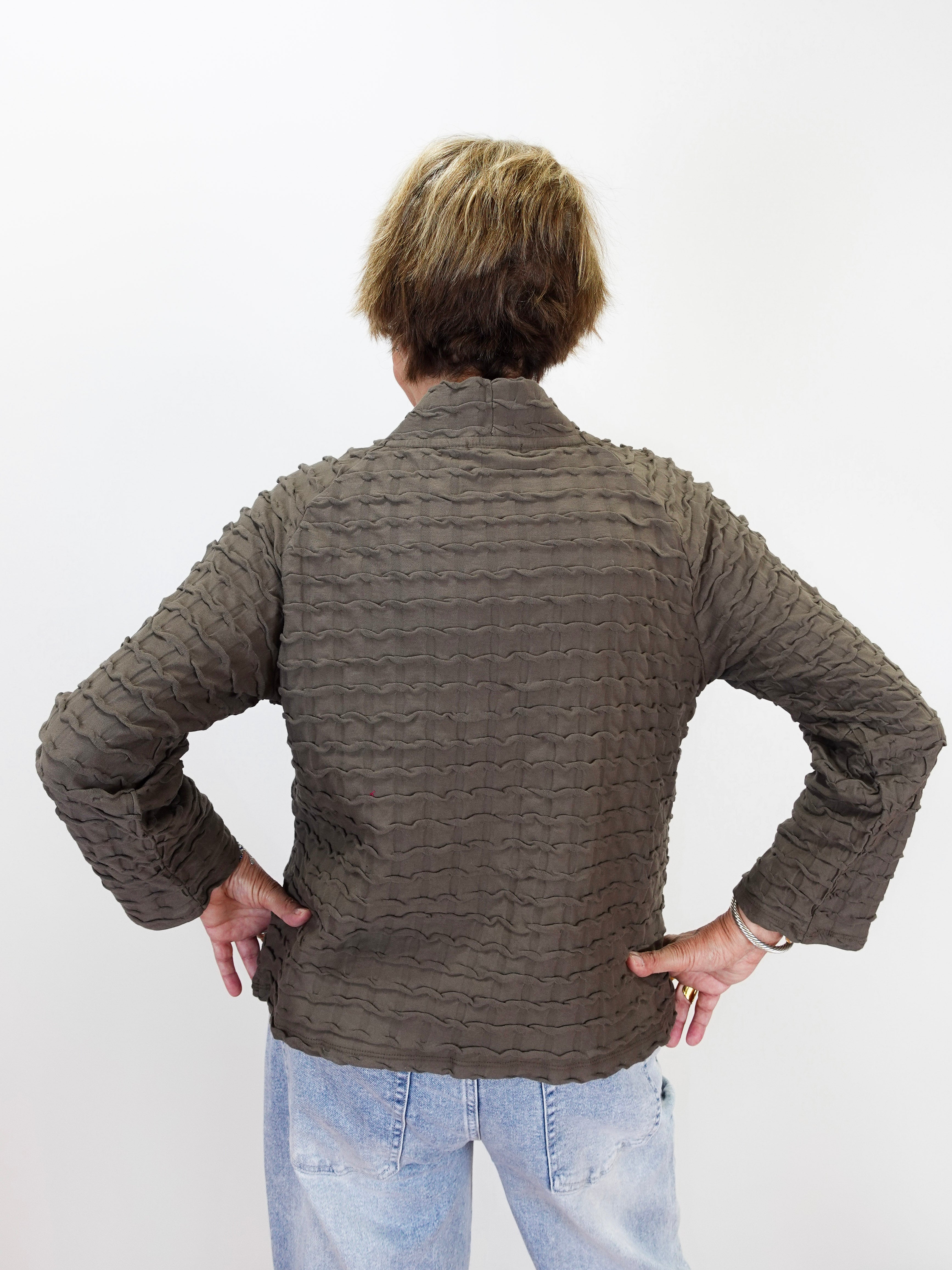 A person viewed from behind wearing a textured, ribbed brown jacket and light blue jeans against a plain white background.