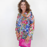 Woman wearing a colorful patterned shirt holding a pink purse against a white background