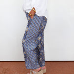 Person wearing blue patterned pants and a white top against a white wall.