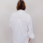 Person wearing a white shirt with rolled-up sleeves against a plain background