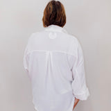 Person wearing a white shirt with rolled-up sleeves against a plain background