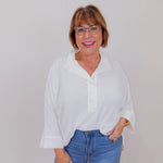 Woman wearing a white blouse and blue jeans against a plain background