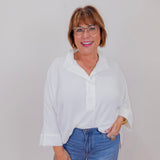 Woman wearing a white blouse and blue jeans against a plain background