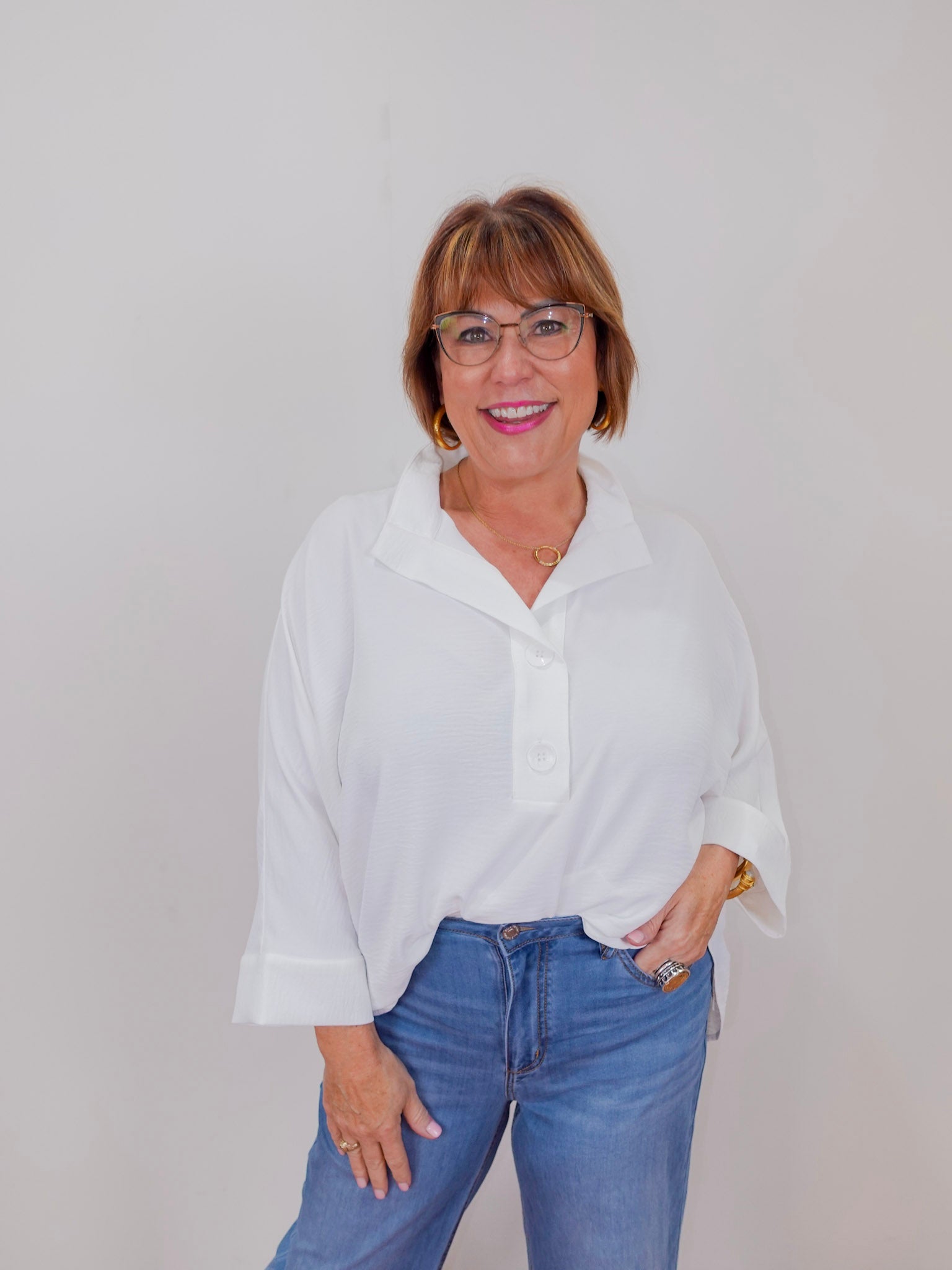 Woman wearing a white blouse and blue jeans against a plain background