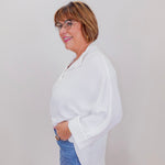 Woman wearing a white blouse and blue jeans against a plain background