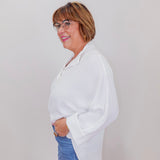 Woman wearing a white blouse and blue jeans against a plain background
