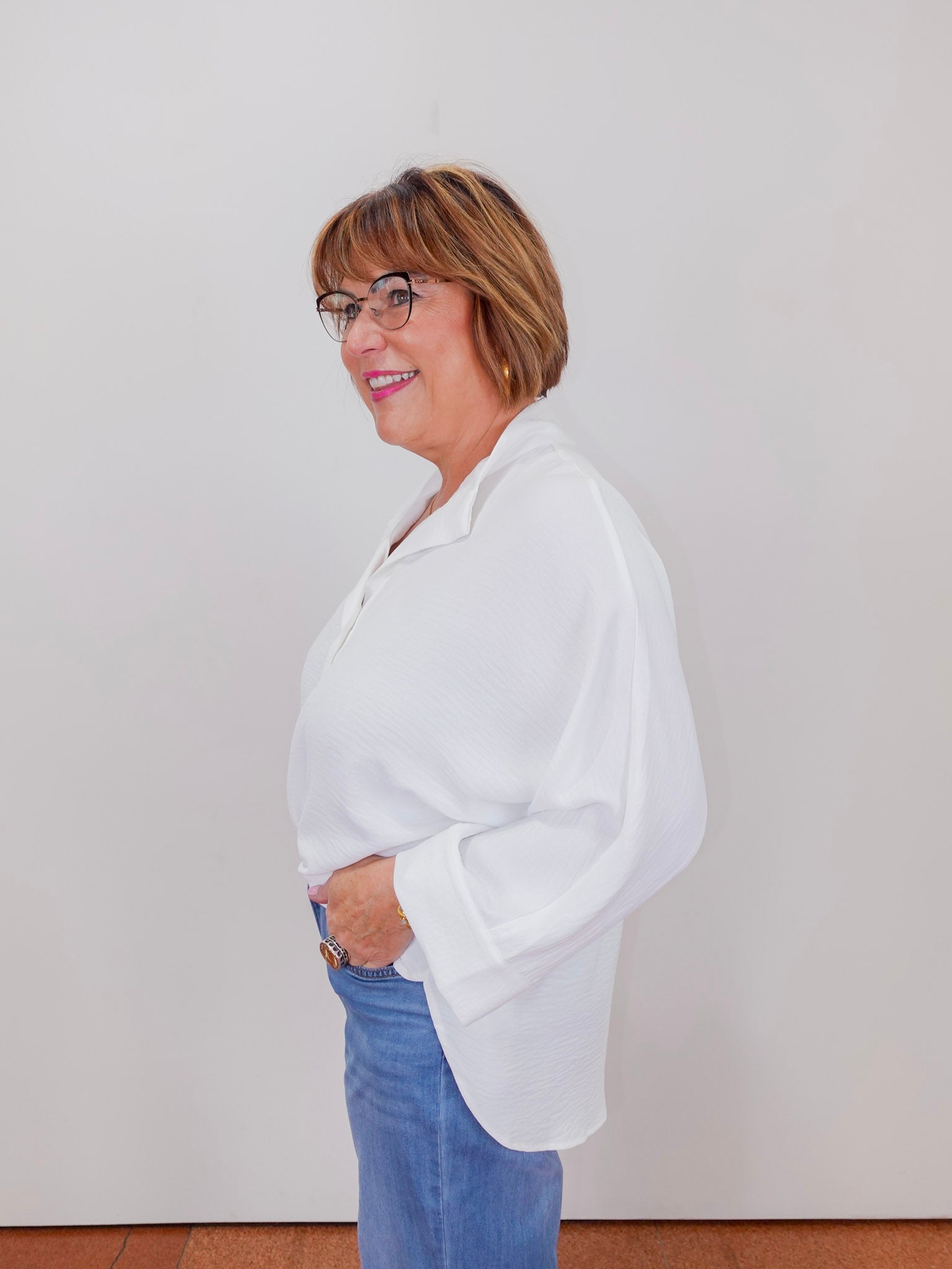 Woman wearing a white blouse and blue jeans against a plain background