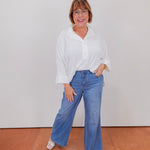Woman wearing a white blouse and blue jeans standing against a plain background