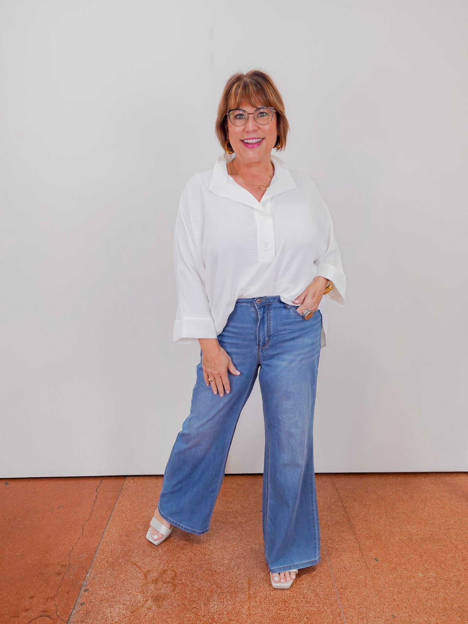 Woman wearing a white blouse and blue jeans standing against a plain background