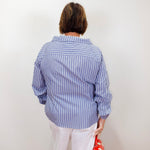 Person wearing a blue and white striped shirt holding a red handbag against a white wall.