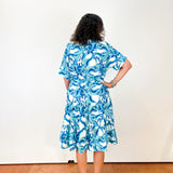 Woman wearing a blue floral dress against a white wall.