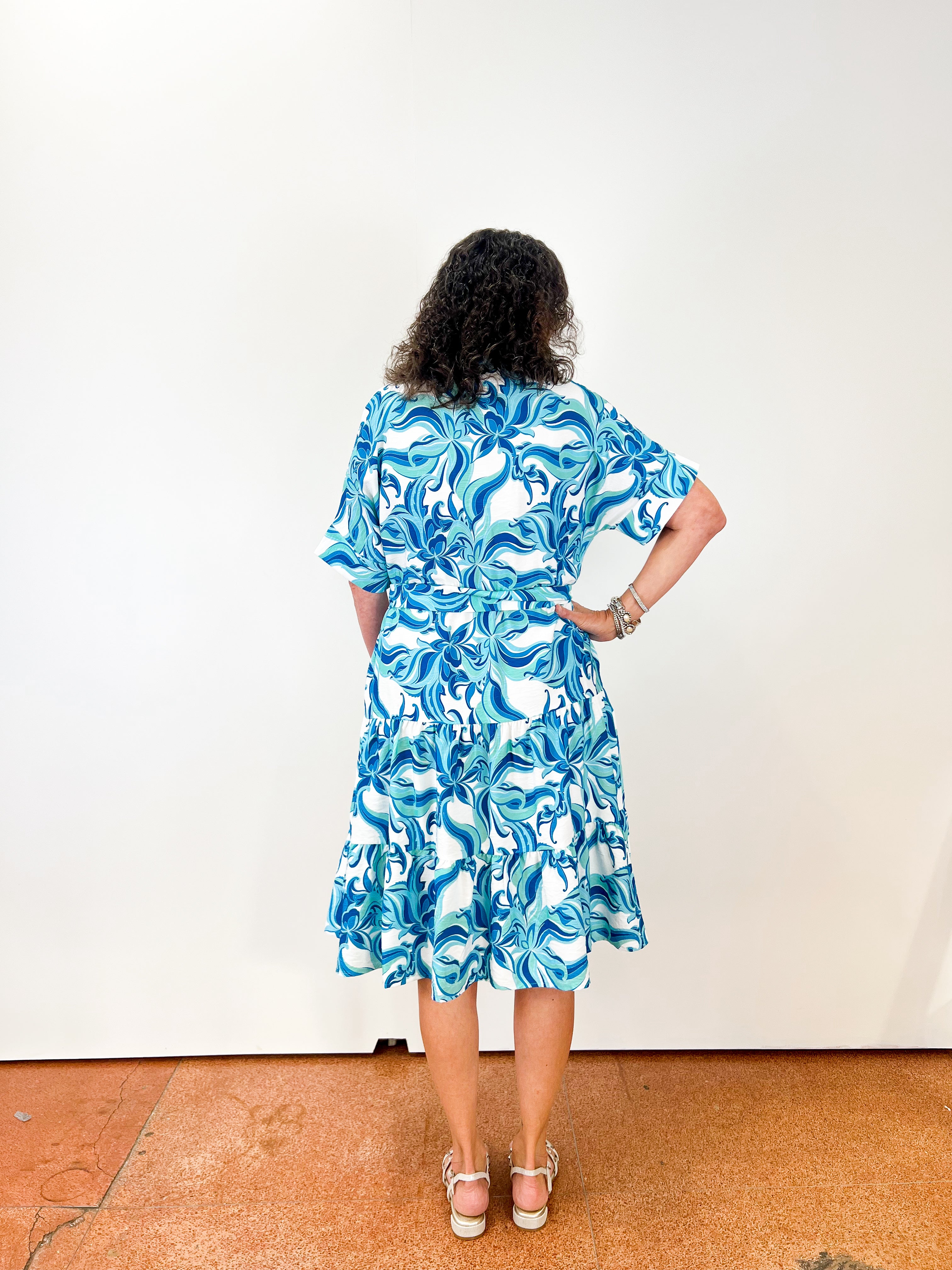 Woman wearing a blue floral dress against a white wall.