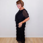 Woman wearing a black dress with sheer sleeves against a white wall.