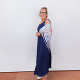 Woman wearing a blue dress with a patterned shawl against a white wall.