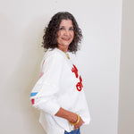 Woman wearing a white sweatshirt with red text and blue jeans against a plain background
