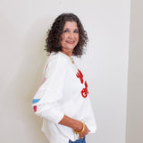 Woman wearing a white sweatshirt with red text and blue jeans against a plain background