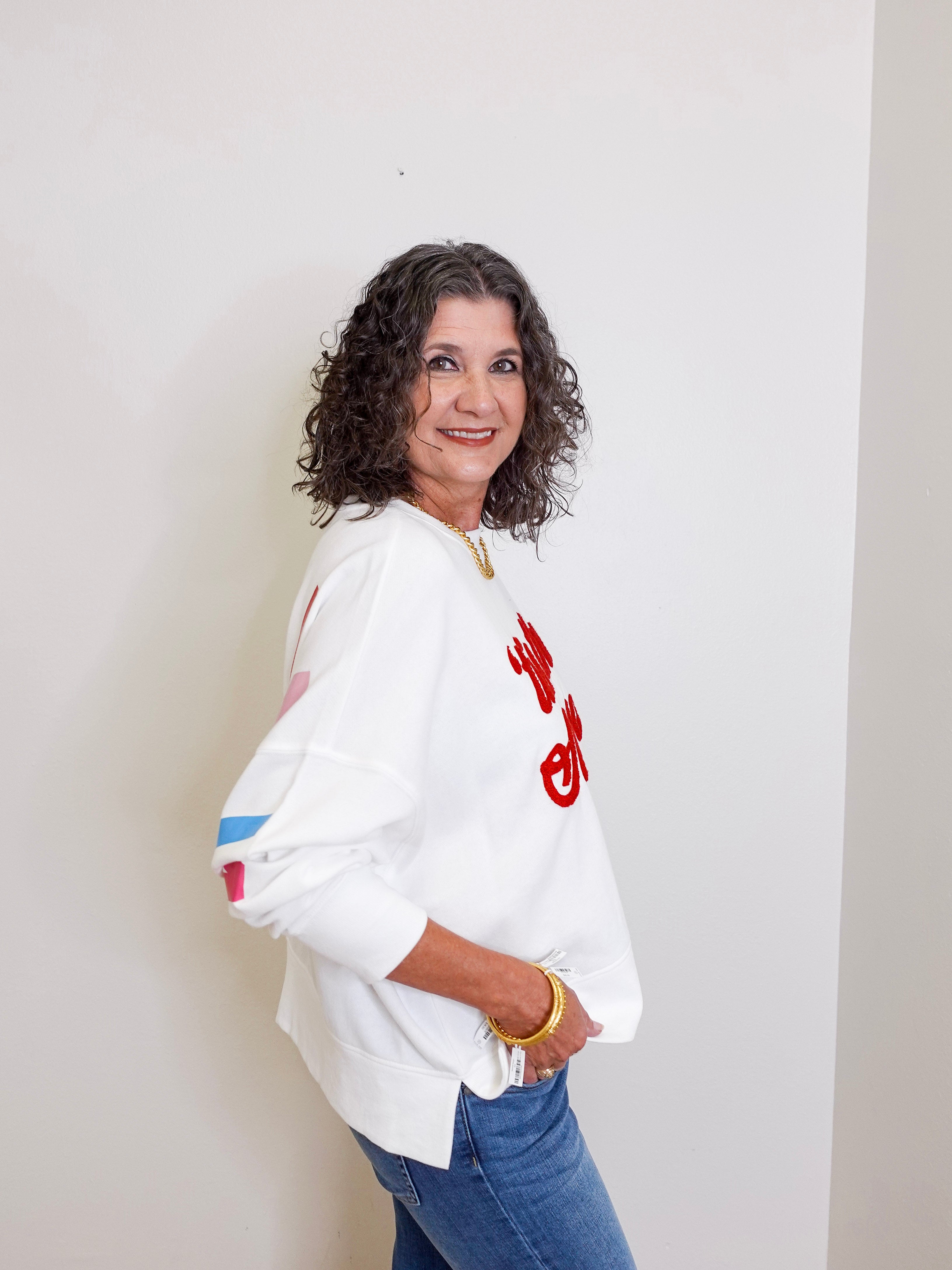 Woman wearing a white sweatshirt with red text and blue jeans against a plain background