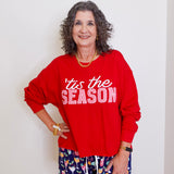 Woman wearing a red 'tis the season sweater and patterned shorts against a white background