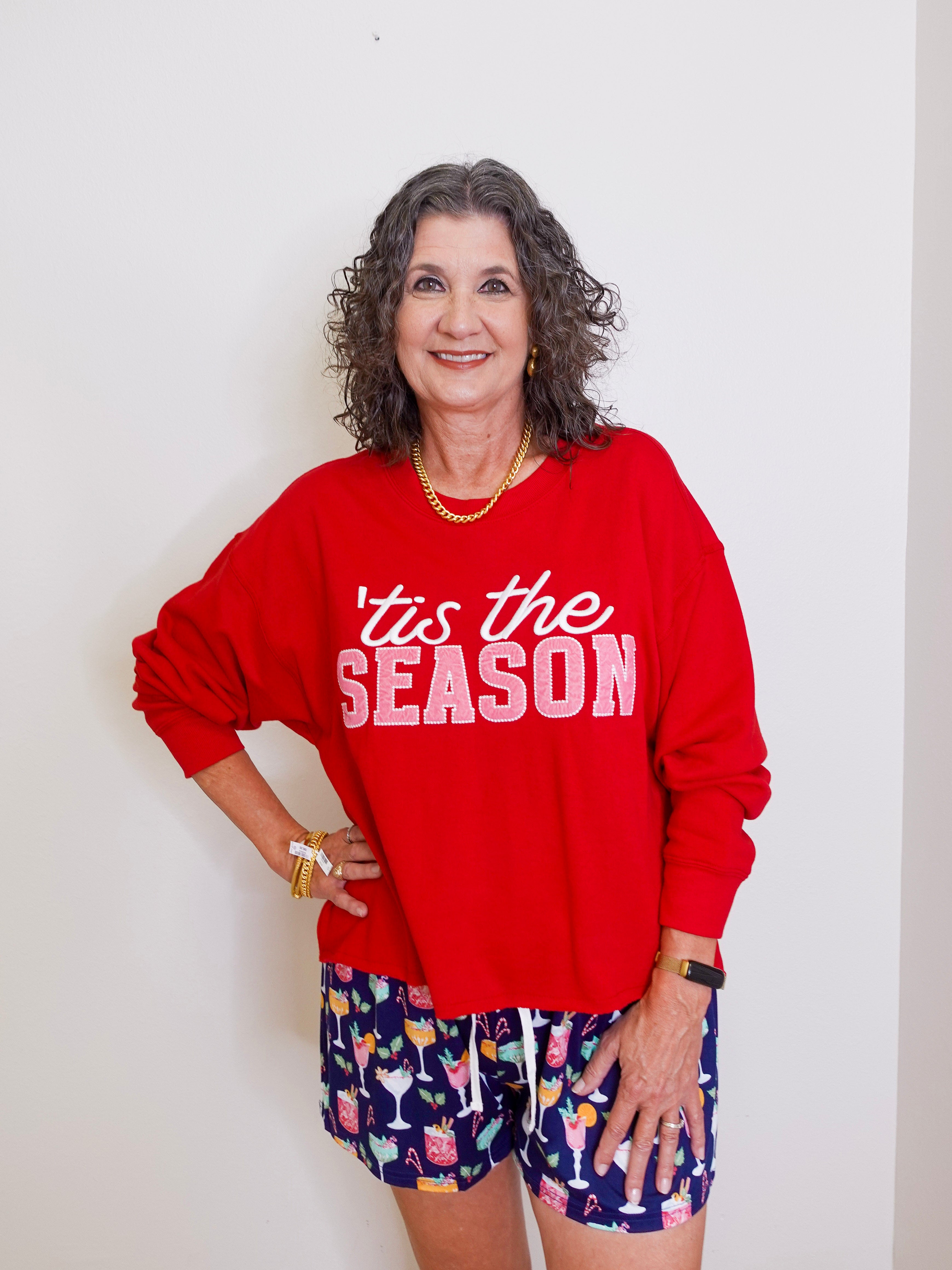 Woman wearing a red 'tis the season sweater and patterned shorts against a white background
