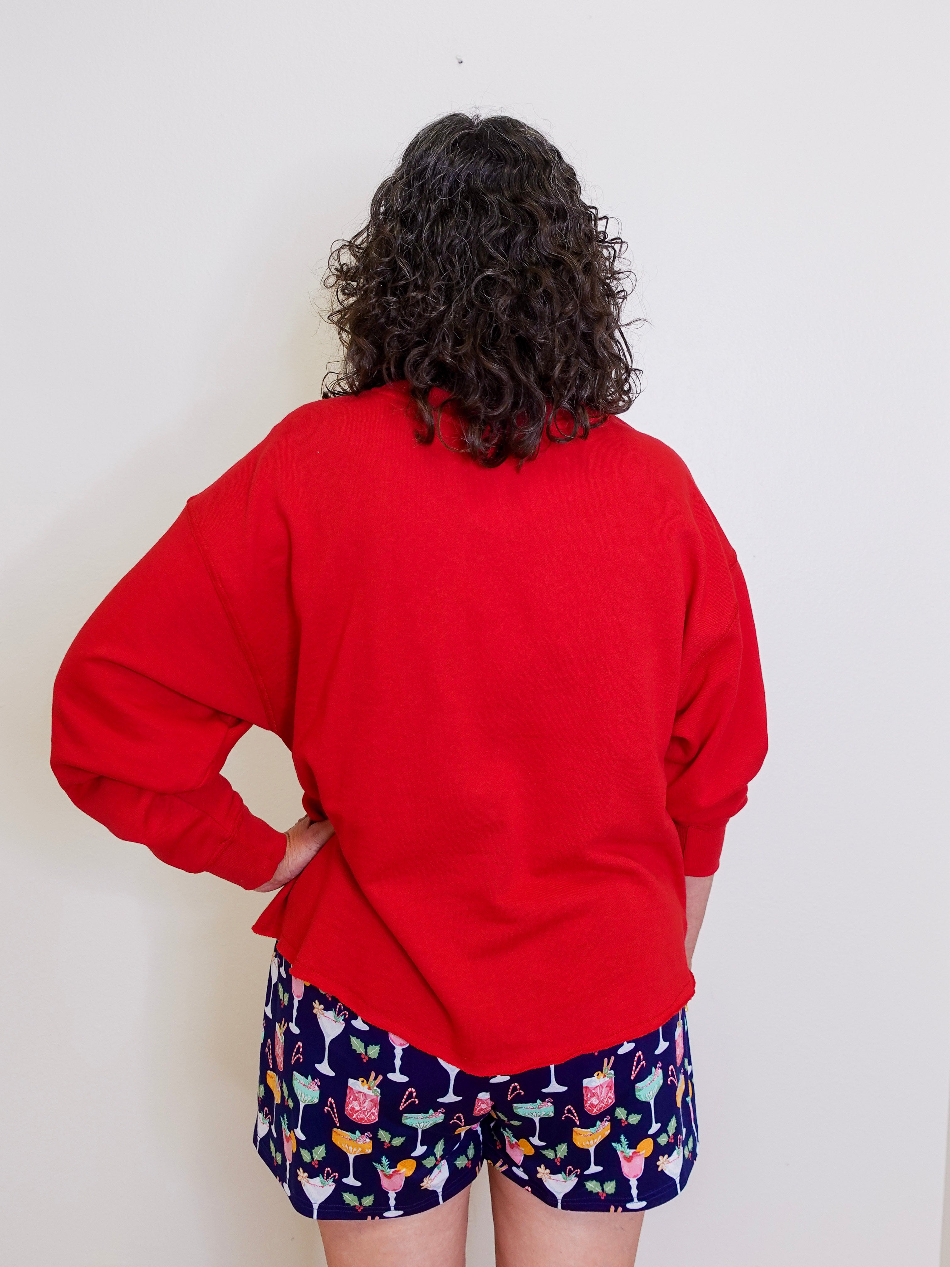 Person wearing a red sweatshirt and colorful shorts against a white background