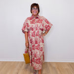 Woman wearing a floral dress standing against a white wall.