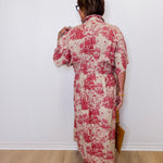 Woman wearing a red and white floral dress against a white wall.