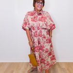 Woman wearing a red and white floral dress holding a yellow handbag against a white wall.