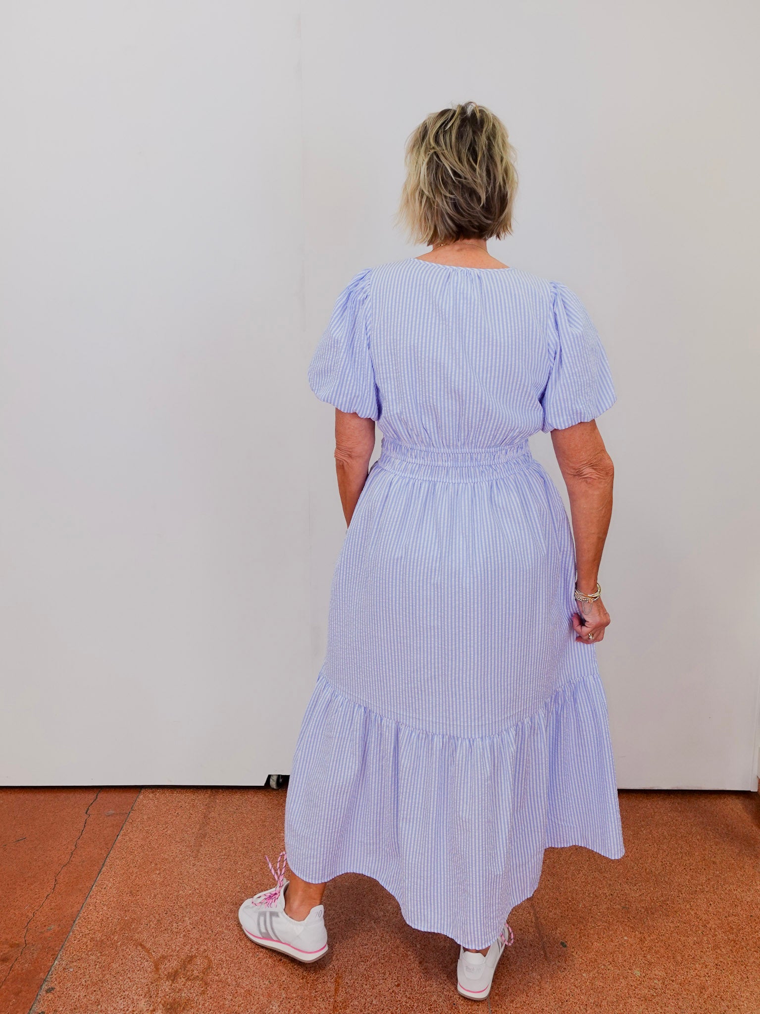 Woman wearing a light blue striped dress standing against a white wall.