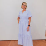 Woman wearing a light blue dress standing against a white wall.