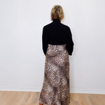 Person wearing a black top and leopard print skirt against a white wall.