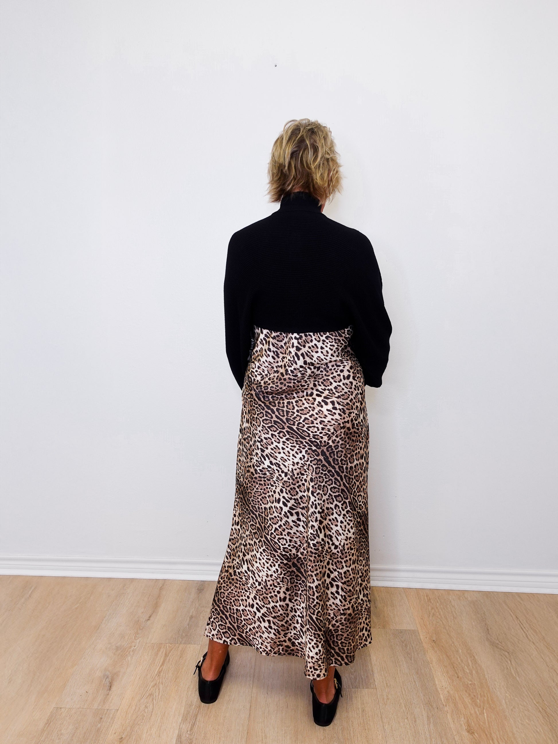 Person wearing a black top and leopard print skirt against a white wall.