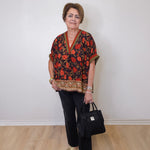 a women wearing a black floral print short sleeve top with black pants and holding a black Brighton purse against a white background 