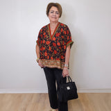 a women wearing a black floral print short sleeve top with black pants and holding a black Brighton purse against a white background 