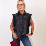 Woman wearing a black ruffled shirt and blue jeans, holding a red handbag against a white background