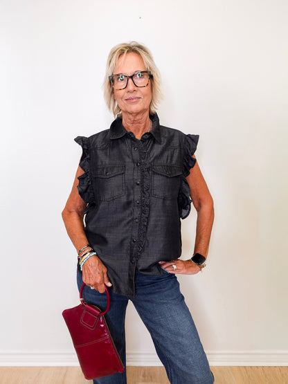 Woman wearing a black ruffled shirt and blue jeans, holding a red handbag against a white background