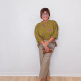 Woman wearing a green patterned sweater and beige pants against a white wall.