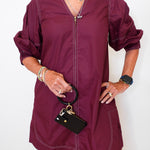 Person wearing a burgundy dress holding a black handbag against a white background