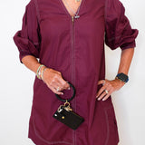 Person wearing a burgundy dress holding a black handbag against a white background