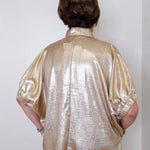 Person wearing a shiny gold shirt against a white wall