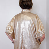 Person wearing a shiny gold shirt against a white wall